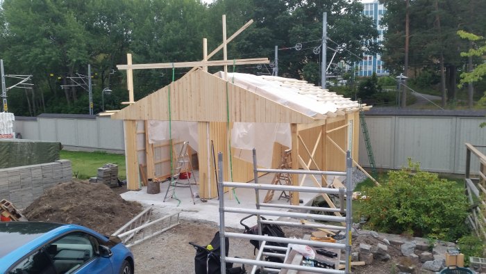 En pågående byggnation av en träkonstruktion med en nyuppsatt gavelspets och en provisorisk ställning av reglar.