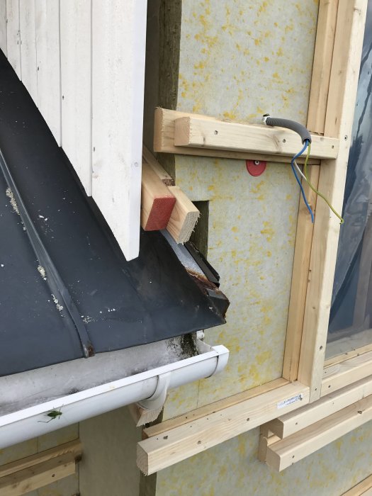 Plåttak möter ny knutbräda på hus med tilläggsisolering och synliga träreglar.