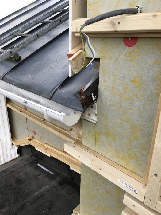 Närbild på en verandabyggnad visar plåttak som möter en ny träknutbräda, med synlig isolering och elkabel.