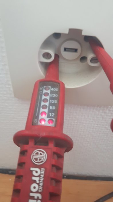 Multimeter tester spänning vid ett perilexuttag, med indikatorlampor lyser för olika voltstyrkor.