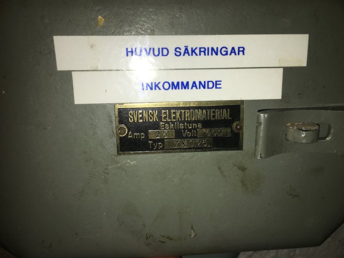 Grå elektrisk låda med etiketter "HUVUD SÄKRINGAR" och "INKOMMANDE", samt en mässingsskylt "SVENSK ELEKTROMATERIAL".