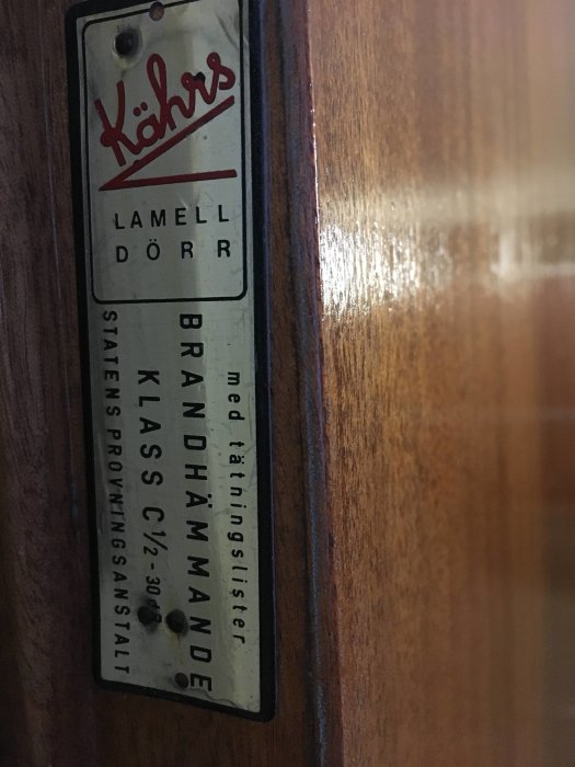 Skylt på dörr med texten "Kährs Lamell Dörr Brandhämmande Klass C12-30" som indikerar brandsäkerhetsklass.