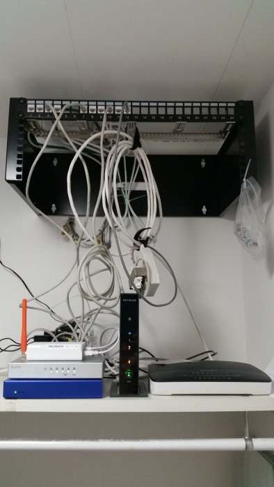 Ett nätverksrack i ett hem med kaotiskt arrangerade kablar, utrustning inklusive en switch och gammalt modem.