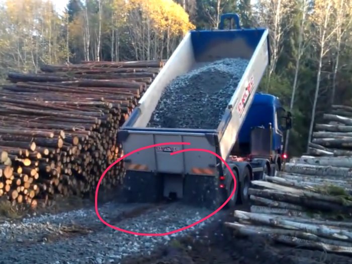 Grusbil tippandes grus i markerade spår med skogsmiljö i bakgrunden.