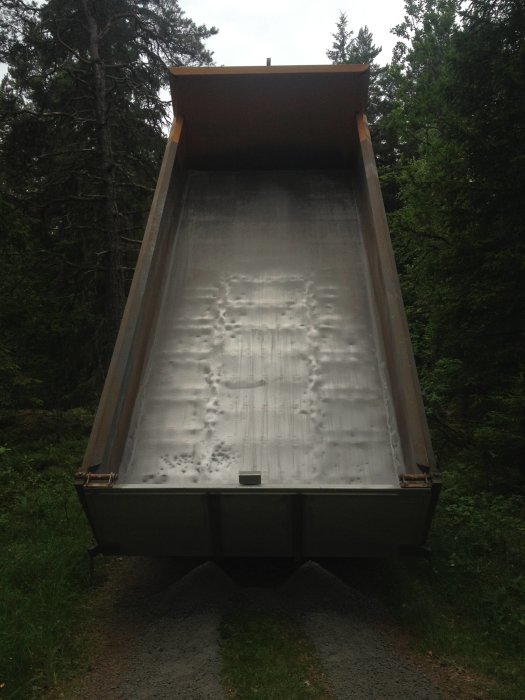 Lastbilens tippflak i skogsmiljö som tömmer ut grus, i färd med att sprida material.