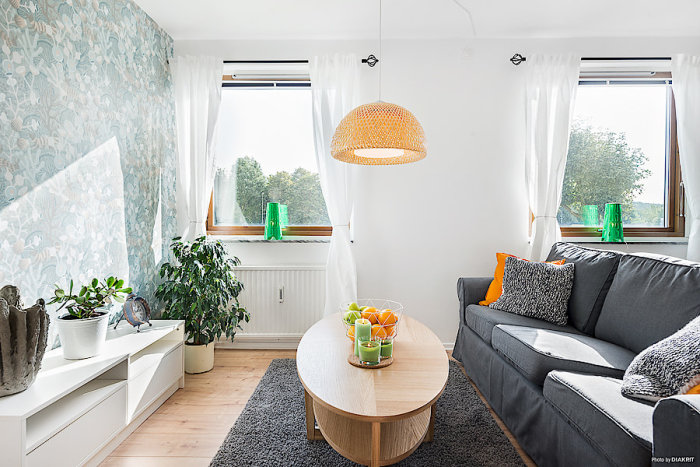 Renoverat modernt vardagsrum med grå soffa, träbord, fondtapet, ljusa väggar och designlampor.