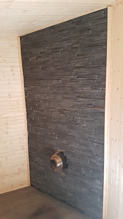 Vägg klädd med äkta sten bakom en kamin i ett bastuförrum, med synlig skorstensgenomföring.