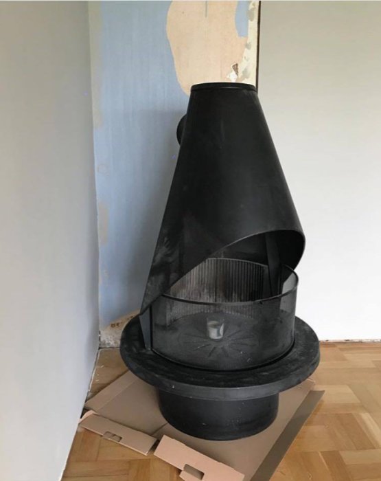 Äldre svart Jøtul öppen spis från 70-talet framför en ljusblå murstock med upptillad kartong under.