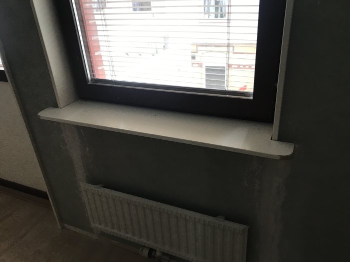 Nyinstallerad infälld fönsterbräda ovanför en radiator, väggar under förberedelse med spackling.