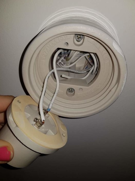 En öppen porslinssockel på en vägg med synliga kablar och en hand som håller en ny lamphållare nära.