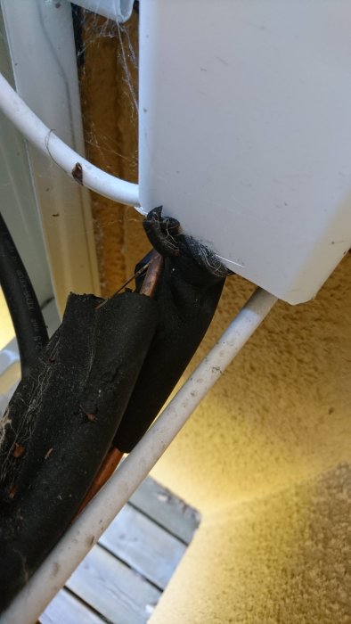Isolering som lossnat på rör vid en luftvärmepumps utedel.