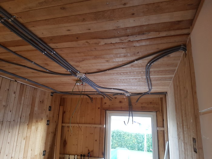Nyinstallerade elledningar i flexrör längs taket i ett rum med träpanelväggar och -tak.
