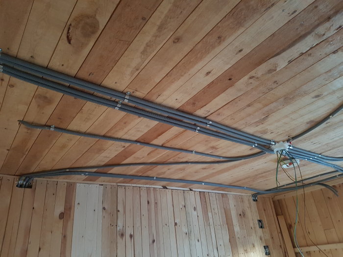 Installation av eldragning i taket med synliga ledningar och kabelrör längs träpaneler.