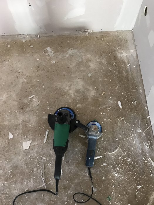 Vinkelslip och slipmaskin på betonggolv med limrester och spackel.