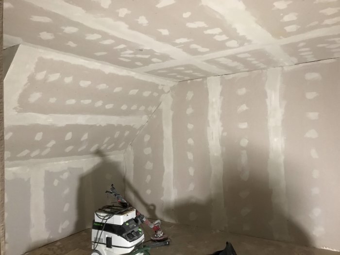 Ett rum med nyspacklade väggar och en golvslipmaskin i förgrunden.