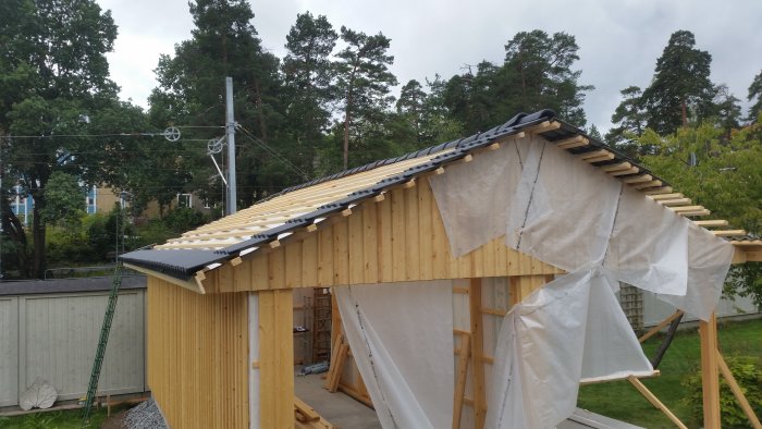 Påbörjat läggning av takpannor på träkonstruktion med några rader längst ner och uppe till höger, under arbete.