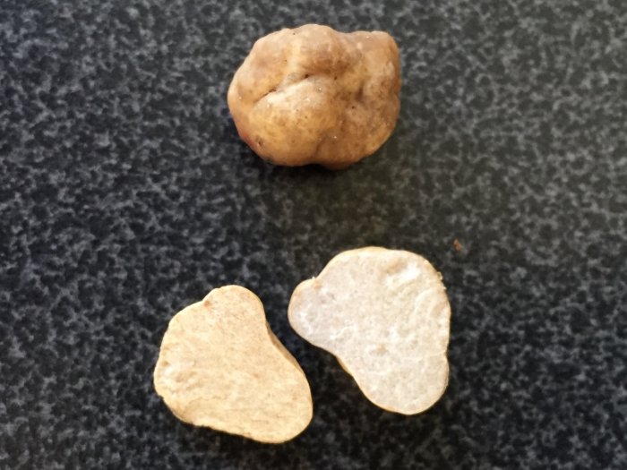 En brun tryffel och två halvor av den på svart bänkskiva.