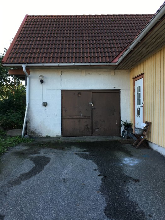 Husfasad med en gammal garageport bredvid en entrédörr, planering av byggtillägg för en entré diskuteras.