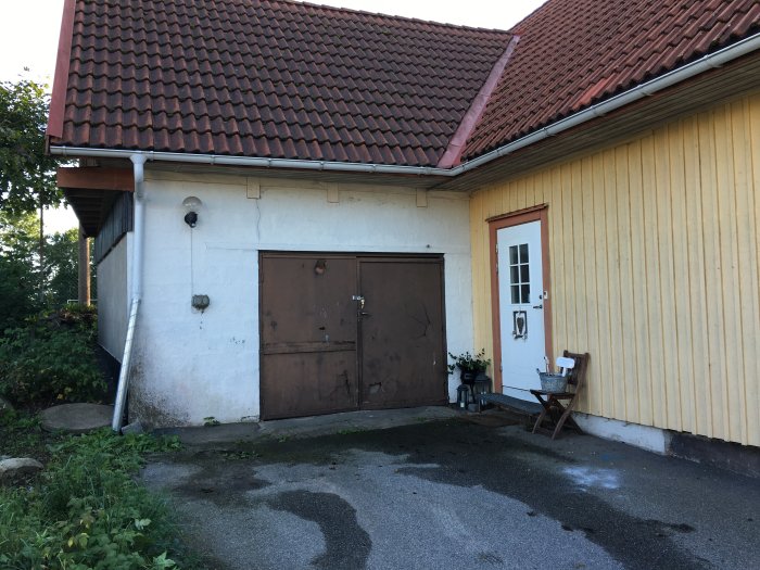 Guldsidig byggnad med ett rött tegeltak, en vit husdörr och en gammal garageport som planeras bli sovrum.