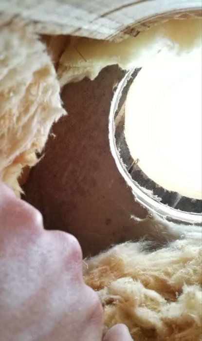 Ventilhål i vägg med synligt vindskyddsgips och isoleringsmaterial, potentiell fuktskada nära fönster.