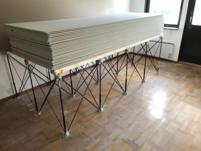 Stapel av gipsskivor på ett uppfällt Centipede arbetsbord i ett dammigt rum under en renovering.