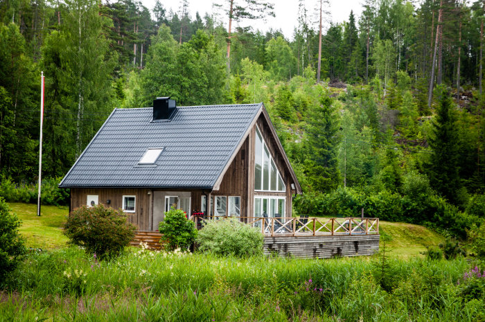 Utbyggd stuga med nyare tillbyggnad och stora fönster i skogsmiljö.