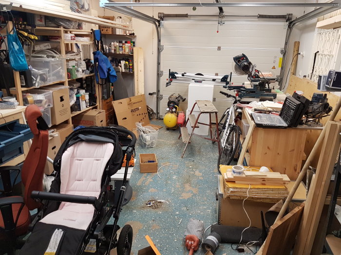 Rörigt garage med diverse verktyg och material utspridda över arbetsytor och golvet.