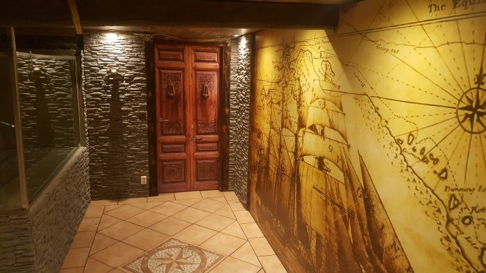 Källarrum med kompassros i natursten på golvet och väggar med kartmotiv och stenstruktur samt en träinristad dörr.