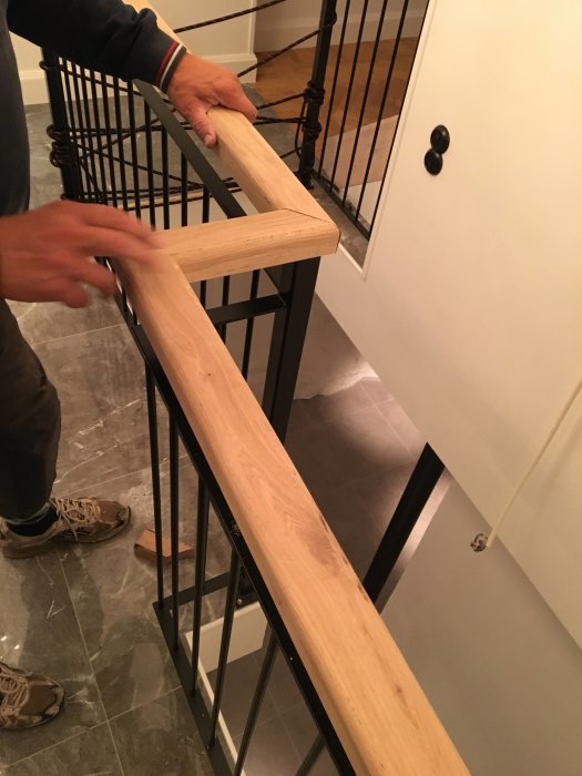 Person installerar en ny hyvlad och fräst ekhandledare på ett svart trappstaket.