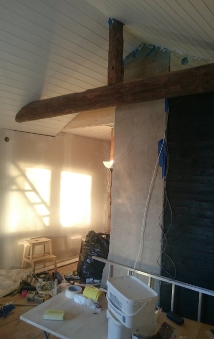 Renoveringsarbete med oavslutad installation av bjälkar och lister, synlig tejp och fogmassa, rörigt bygge.