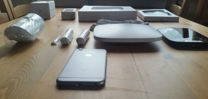 Hemlarmssystem och dess komponenter utspridda på ett träbord, jämfört med en iPhone för storleksreferens.