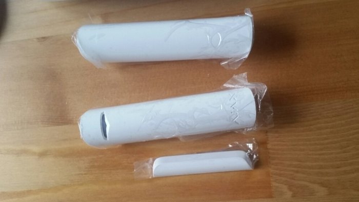 Två större larmenheter och en mindre magnetkontakt inslagna i plast, på ett träbord.