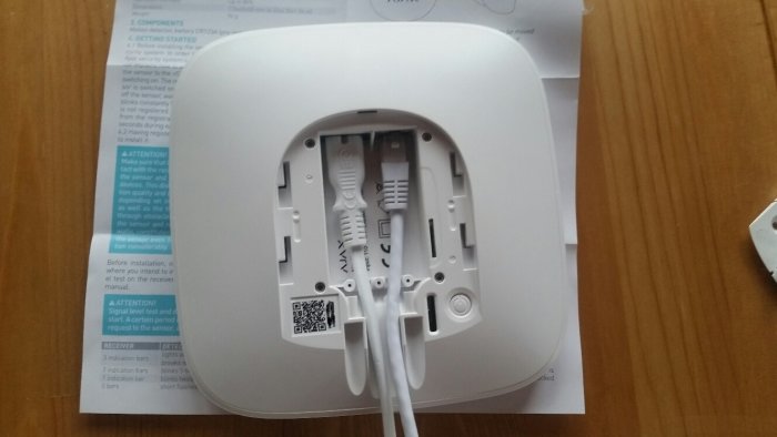 Baksidan av ett larmenhets hölje med nätverkskablar anslutna och QR-kod synlig.