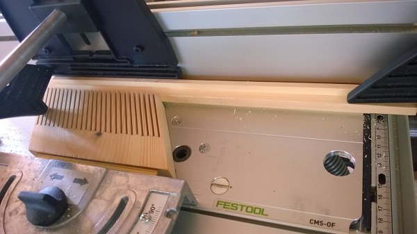 Trästycke med frästa spår nära en Featherboard och Festool fräsbord, visar manuell precision i träarbete.