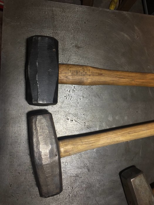 Två olika modeller av 5-kg släggor med trähandtag, en slank och en bredare, på metallunderlag.