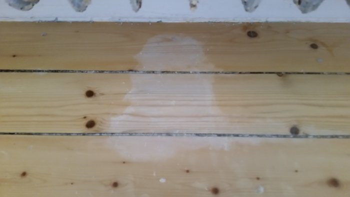 Trägolv med avlägsnad färg under radiator efter oväntad färgborttagningsdropp.