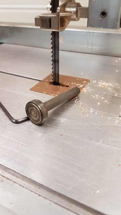 Axel med kullager från en bandsåg av märket Scheppach, liggande på en sågbord med sågspån.