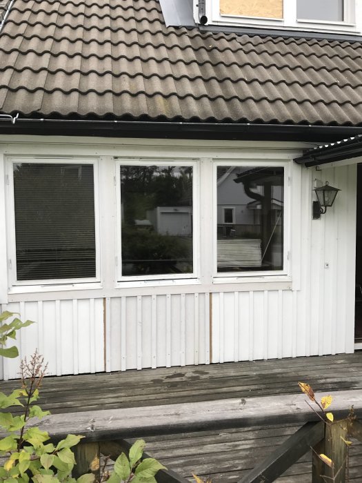Husfasad efter renovering med nya fönster och en borttagen dörr, arbetsredskap syns i bakgrunden.