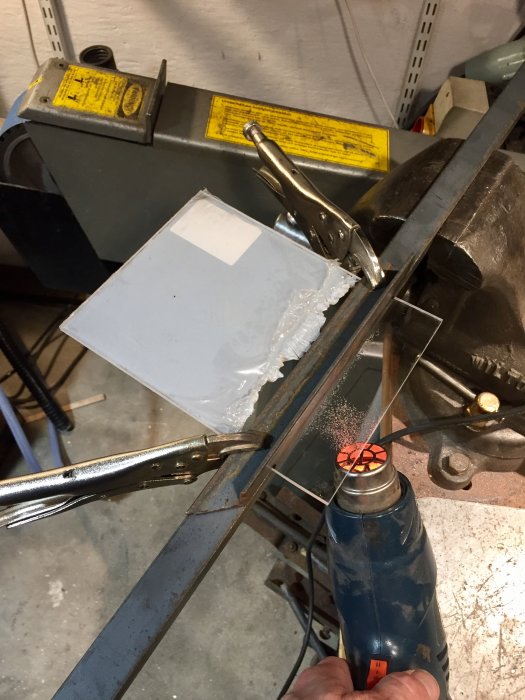 Svetsning av plexiglas stänkskydd på verkstadsbänk med tång och värmeverktyg.