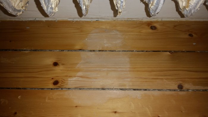 Träpanel med avslipade områden och spår av äldre lack som belyses med blixt.