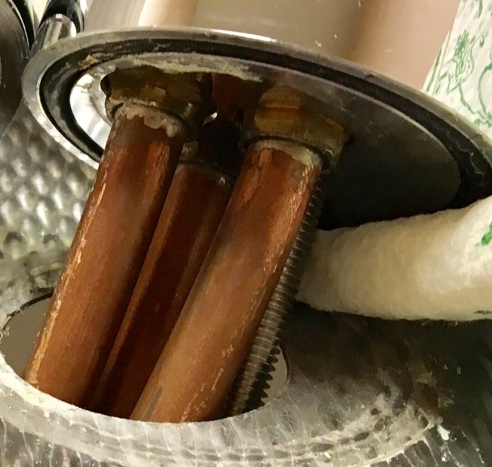 Undersida av köksblandare med kopparledningar och små muttrar, monterade under diskbänken.