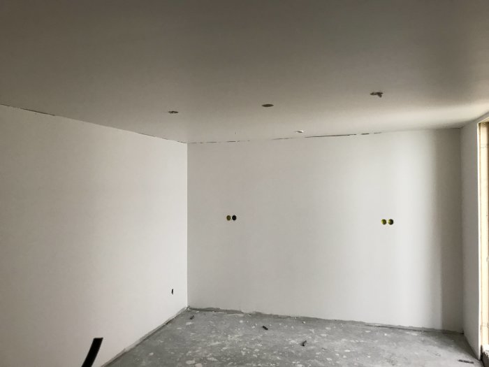 Nymålat förråd med vita väggar och tak, tomma kabeluttag på väggen, betonggolv med spår av byggdamm.