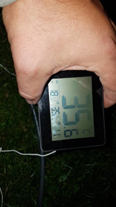 En hand håller en digital termometer som visar 58 grader Celsius, vilket indikerar effekten på kaminens värmeöverföring.