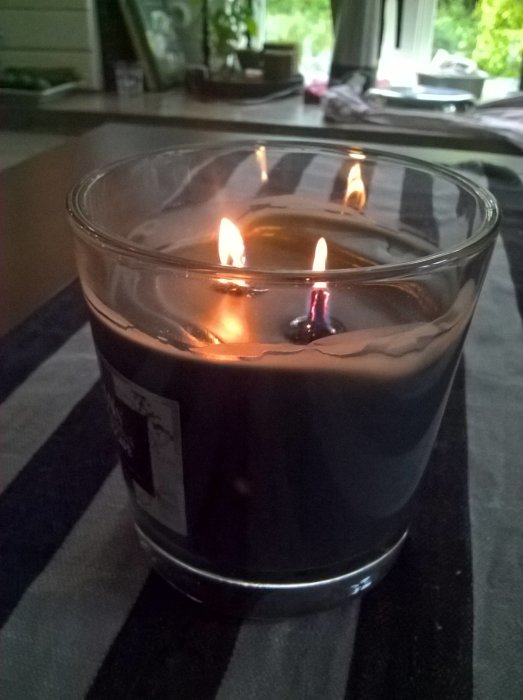 Tänd doftljus i glasbehållare på bord med suddig trädgårdsbakgrund.