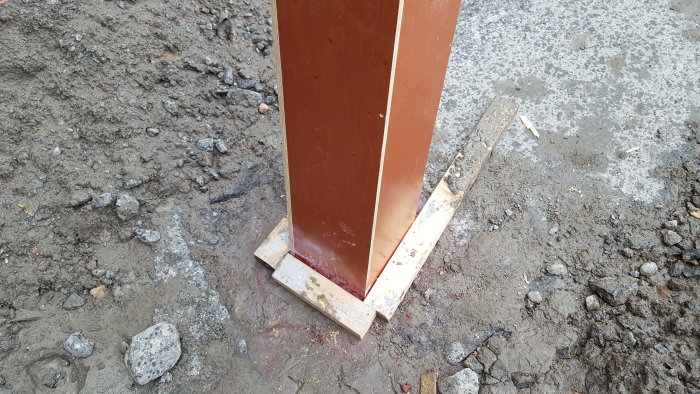 En gjutform för betong stabiliserad med reglar på en grusig markyta, redo för förstärkning.