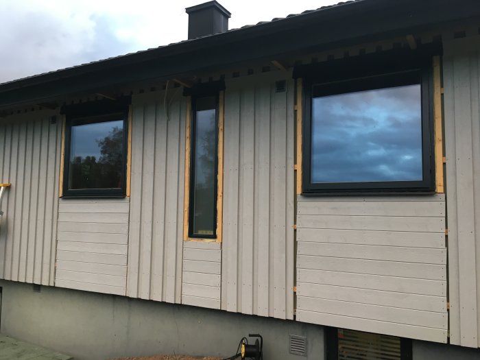 Nyligen installerade fönster på en grå husfasad med reflekterande himmel.