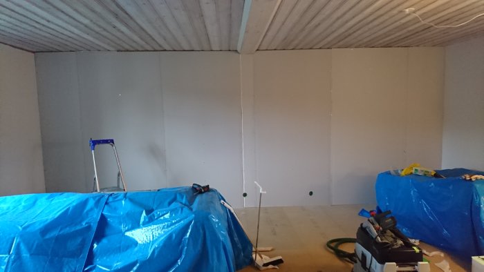 Half-installed drywall with visible seams in a room under construction, tools, and a ladder visible.