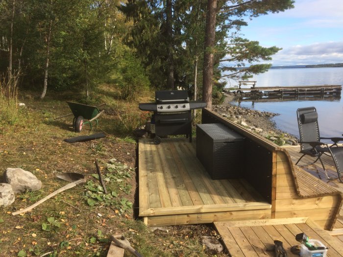 Nytt utelkök och dynlåda bakom soffa på träaltan vid sjö med verktyg i förgrunden.