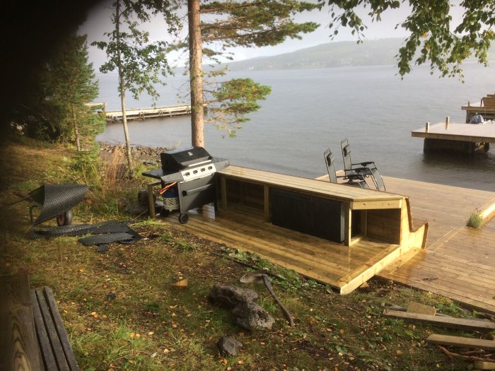 Nytt utelkök och dynlåda byggt av trä bakom utomhussoffa vid en sjö med brygga i bakgrunden.