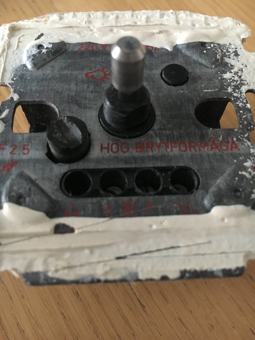 Närbild av en använd elektrisk dimmer för vägginstallation med tydliga tecken på slitage.